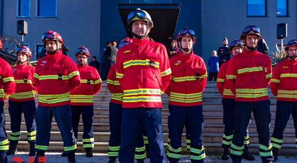 Grupo de bombeiros em uniforme vermelho e amarelo, em formação.