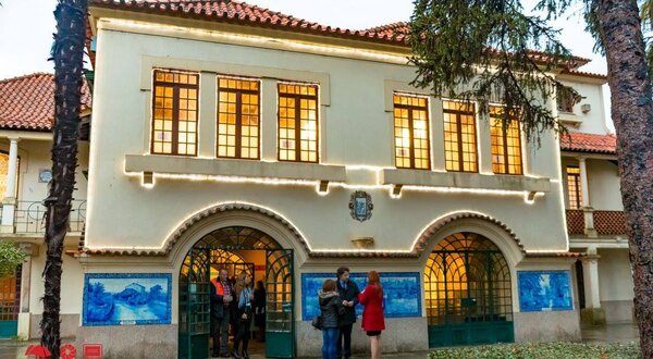 Edifício histórico com janelas grandes e pessoas à entrada, decorado com luzes.