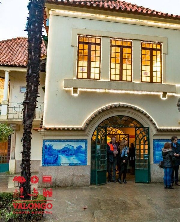 Edifício histórico com janelas grandes e pessoas à entrada, decorado com luzes.