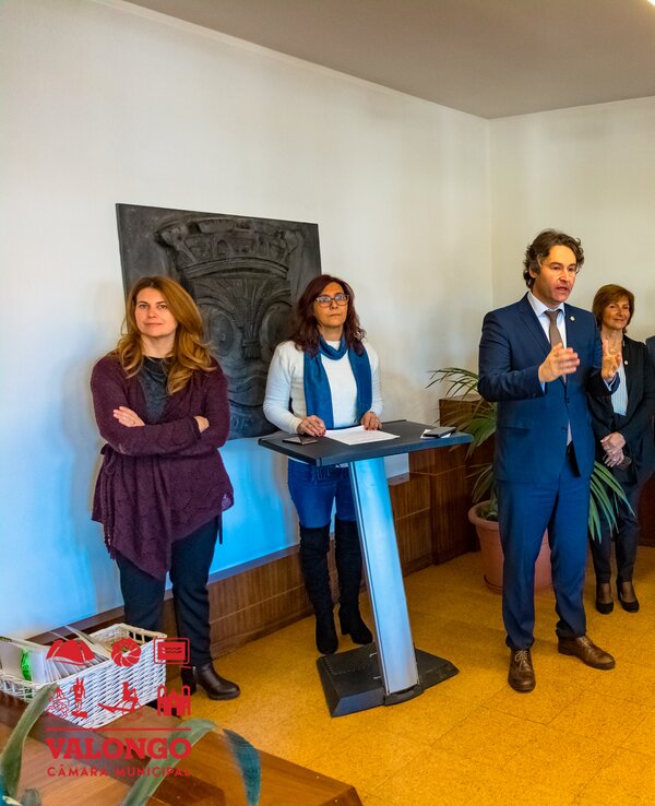 Grupo de pessoas em uma sala, com um orador em destaque ao centro.