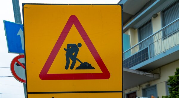 Placa amarela triangular a indicar o início de obras na via pública.