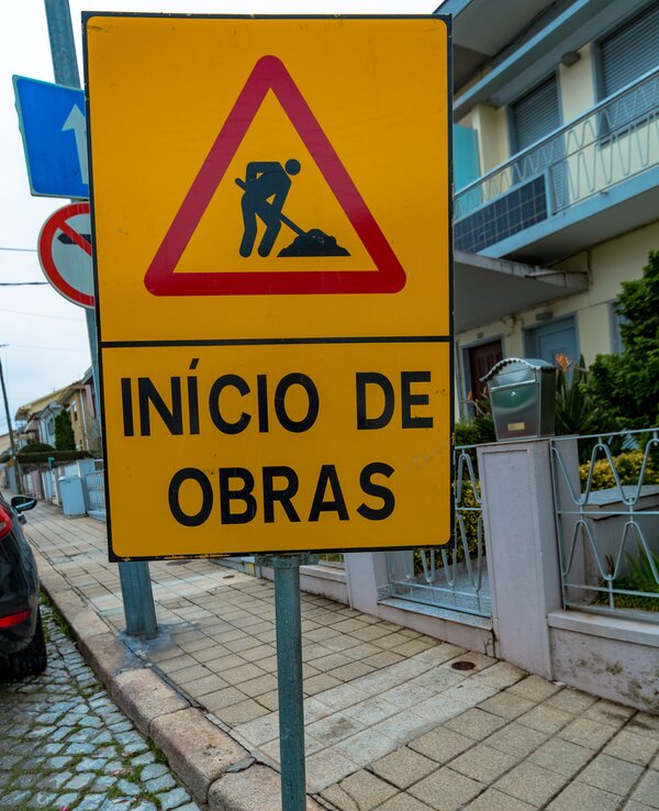 Placa amarela triangular a indicar o início de obras na via pública.