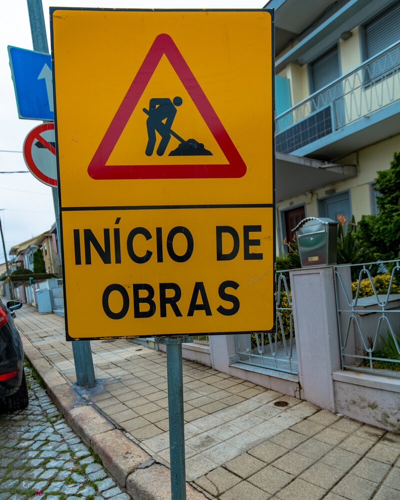 Placa amarela triangular a indicar o início de obras na via pública.