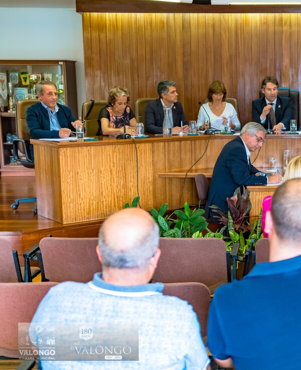 Reunião formal com várias pessoas sentadas à mesa em ambiente institucional.