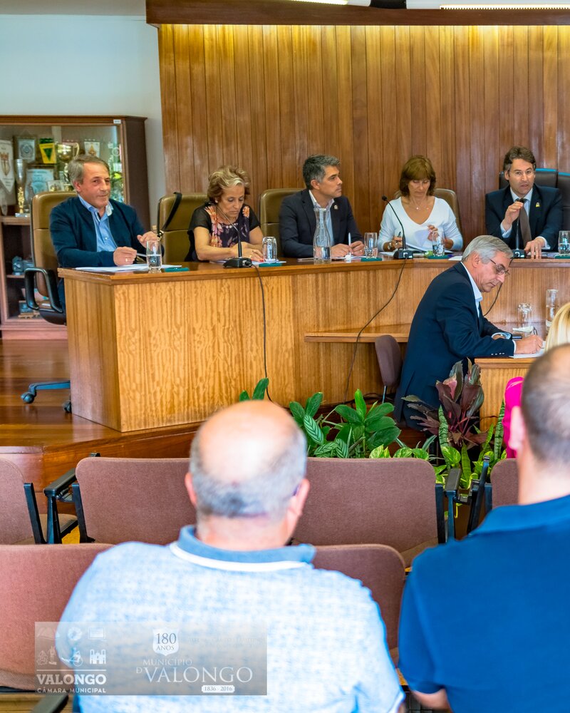 Reunião formal com várias pessoas sentadas à mesa em ambiente institucional.