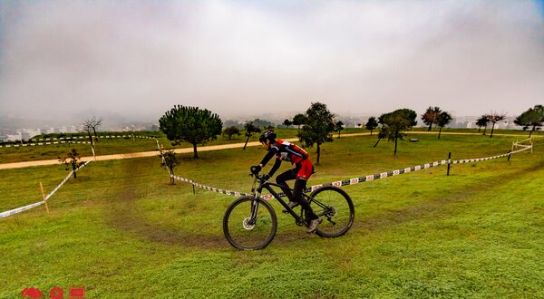 Ciclista a pedalar numa pista de terra, rodeado de árvores e nevoeiro.