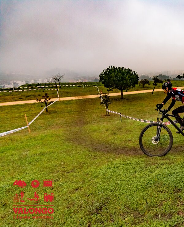 Ciclista a pedalar numa pista de terra, rodeado de árvores e nevoeiro.