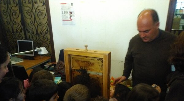 Um grupo de crianças observa um painel de apicultura com um adulto.