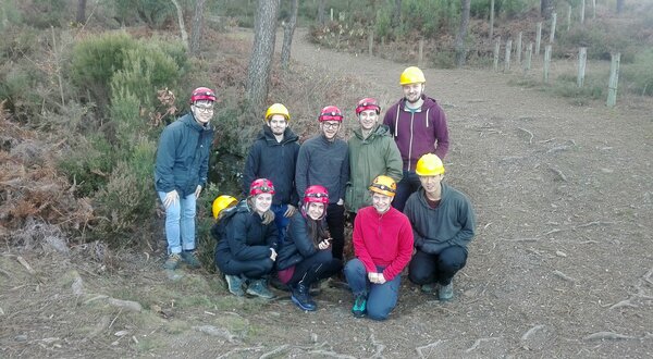Grupo de nove pessoas em ambiente natural, usando capacetes amarelos e vermelhos.