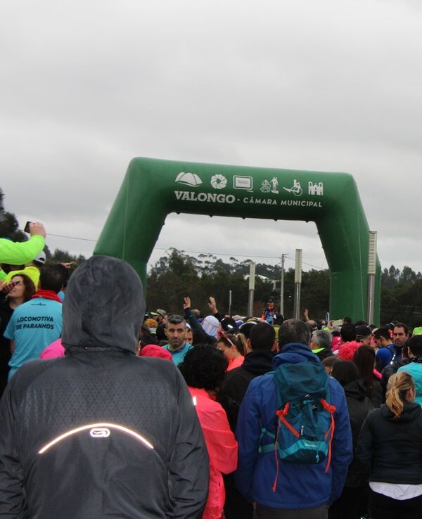Multidão reunida sob um arco verde de partida em Valongo, dia nublado.