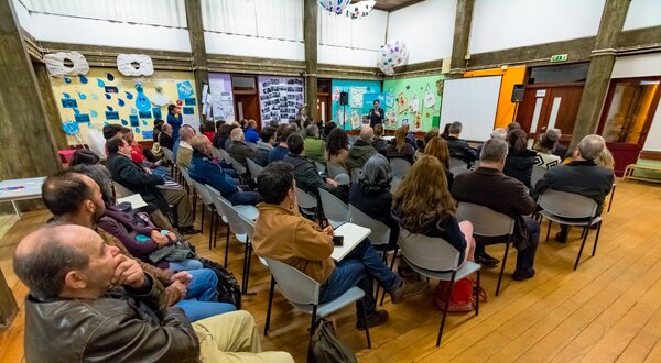 Público atento a uma apresentação em sala com decoração colorida.