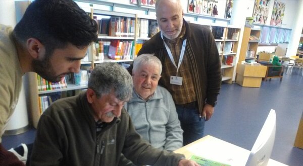 Grupo de pessoas a aprender a usar um computador numa biblioteca.