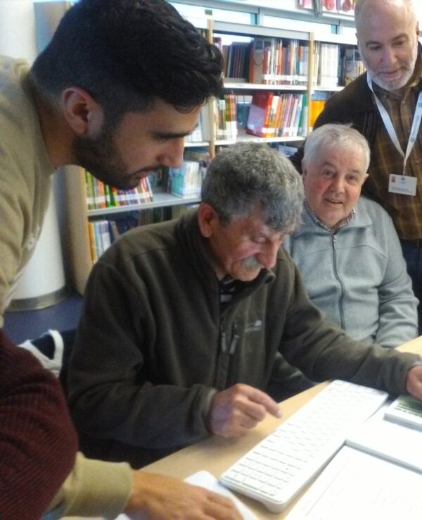 Grupo de pessoas a aprender a usar um computador numa biblioteca.