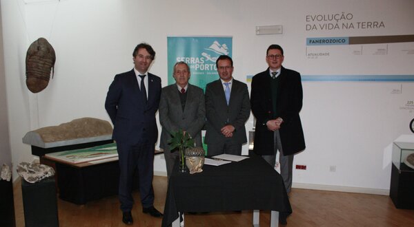 Quatro homens em trajes formais posam ao lado de uma mesa com plantas.