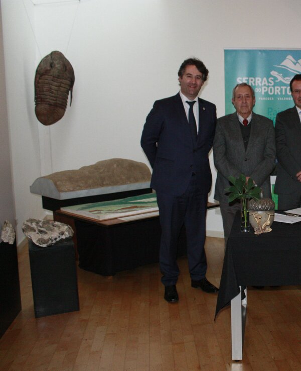 Quatro homens em trajes formais posam ao lado de uma mesa com plantas.