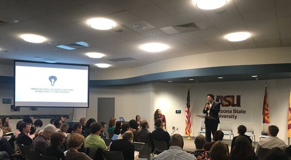 Palestra com público atento na Arizona State University, apresentador em destaque.