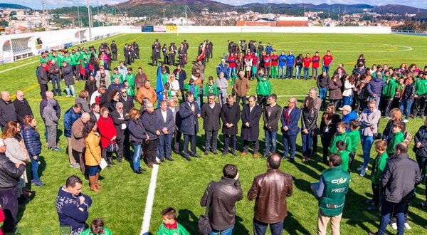 Grupo de pessoas reunidas num campo de futebol, com bandeiras e uniformes.