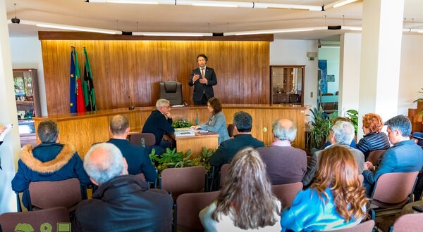 Reunião em Valongo com várias pessoas a ouvir um orador no palco.