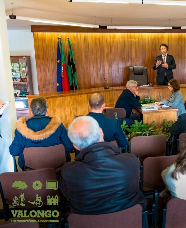 Reunião em Valongo com várias pessoas a ouvir um orador no palco.