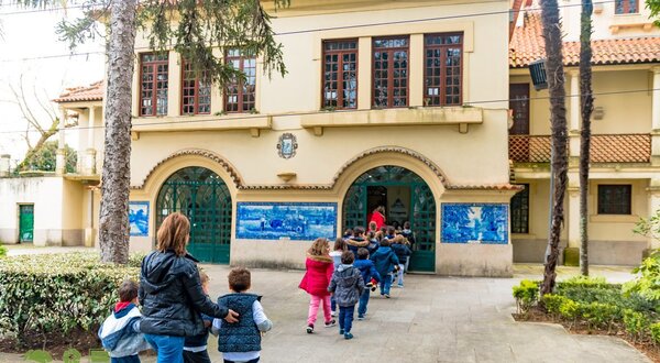 Grupo de crianças a entrar numa escola, acompanhadas por um adulto.