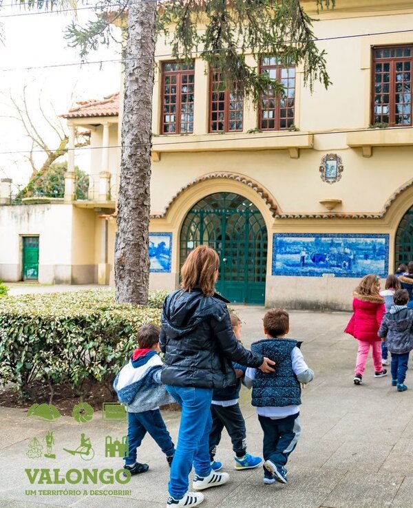 Grupo de crianças a entrar numa escola, acompanhadas por um adulto.
