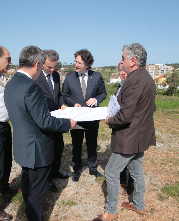 Grupo de homens a discutir um projeto ao ar livre, com plantas na mão.