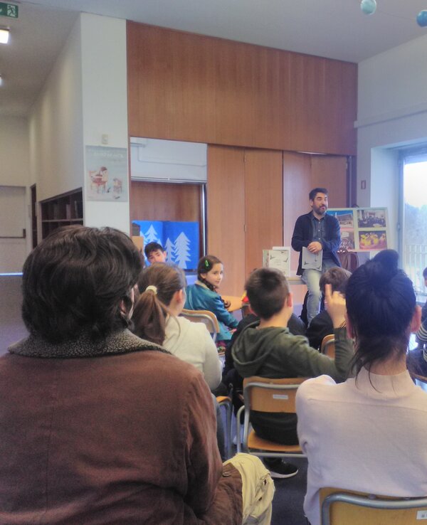 Um grupo de crianças e adultos numa sala, ouvindo um orador.