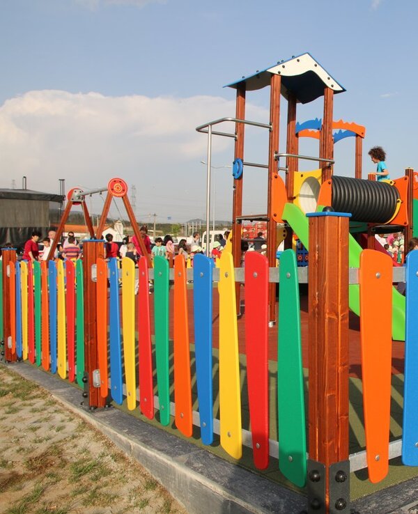 Parque infantil colorido com cercas vibrantes e crianças a brincar.