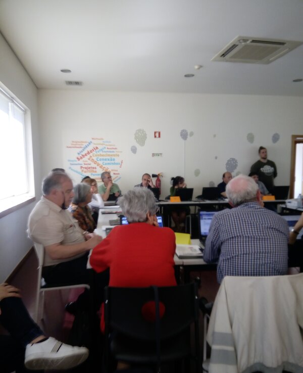 Grupo de pessoas em sala de aula, com computadores e um orador à frente.