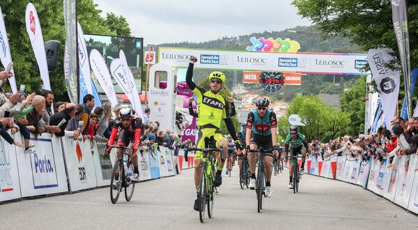 Ciclista em amarelo celebra a vitória na linha de chegada, com público animado.