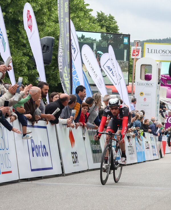 Ciclista em amarelo celebra a vitória na linha de chegada, com público animado.