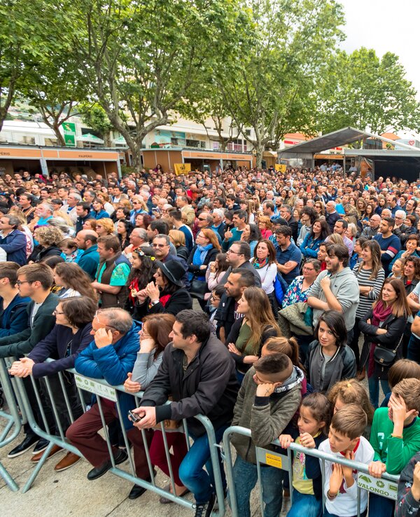 Multidão de pessoas reunidas em um evento ao ar livre, com barracas ao fundo.