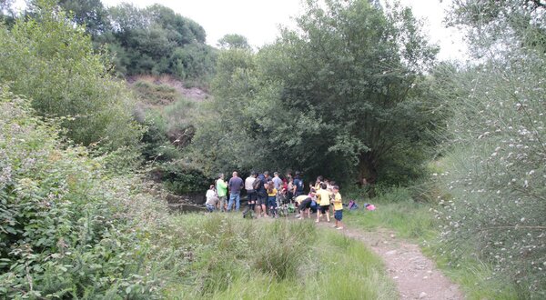 Grupo de pessoas reunidas à beira de um riacho, rodeadas por vegetação.