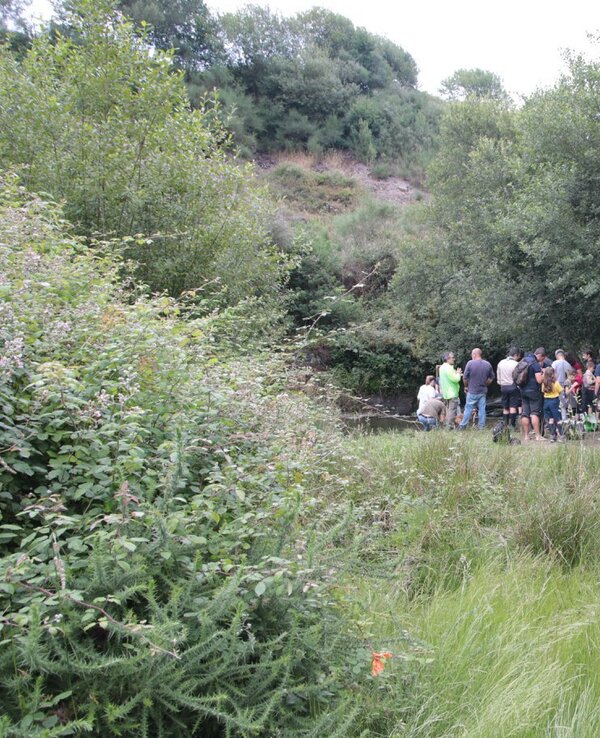 Grupo de pessoas reunidas à beira de um riacho, rodeadas por vegetação.