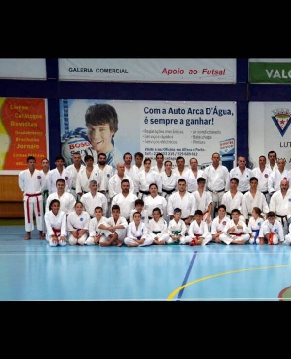 Grupo de praticantes de karaté em uniforme branco, posando em um pavilhão desportivo.