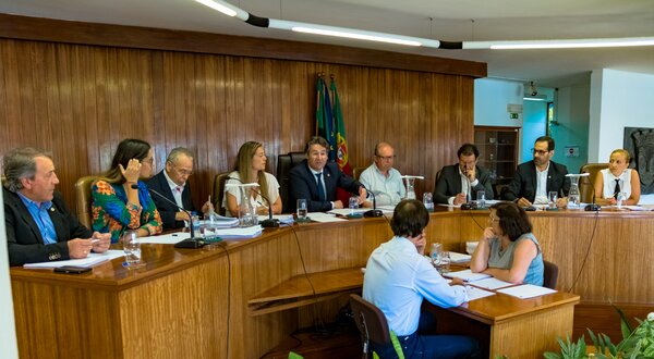 Reunião formal com várias pessoas sentadas à volta de uma mesa em ambiente institucional.