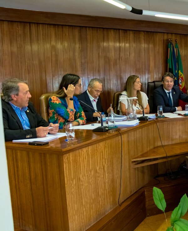 Reunião formal com várias pessoas sentadas à volta de uma mesa em ambiente institucional.