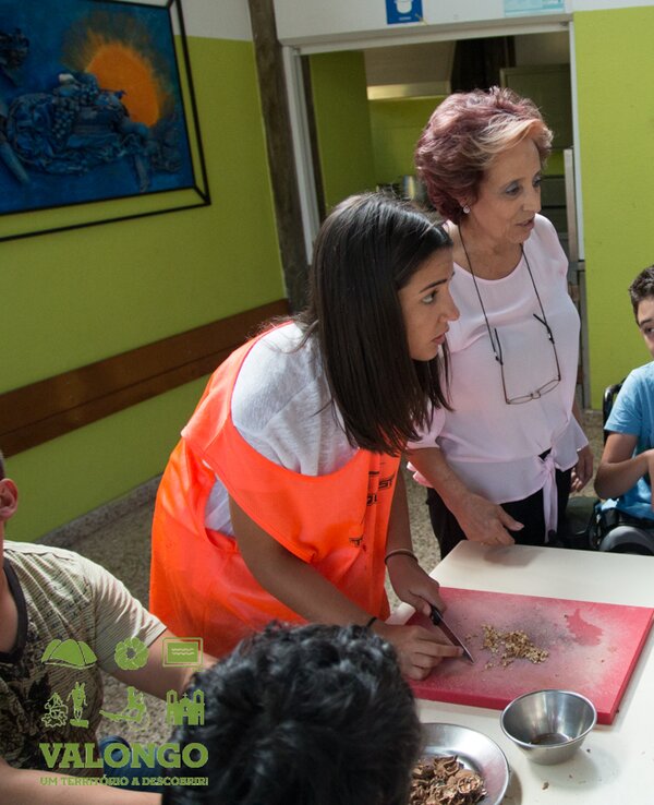 Grupo de crianças e adultos a preparar alimentos numa mesa de cozinha.