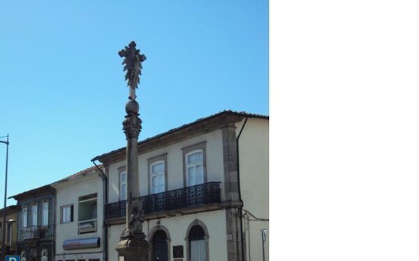 Monumento com coluna ornamentada numa praça, junto a edifícios históricos.